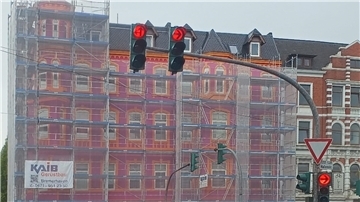 Das Haus in der Hafenstraße Ecke Eupener Straße mit dem ersten, lila-orangefarbenen Anstrich, der trotz des Gerüstnetzes gut erkennbar ist. Das Haus wurde danach neu gestrichen.