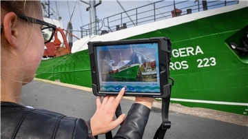 Eine junge Frau bedient ein Tablet vor einem Schiff.