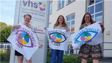 Drei Frauen halten Plakate von der interkulturellen Woche in den Händen. 