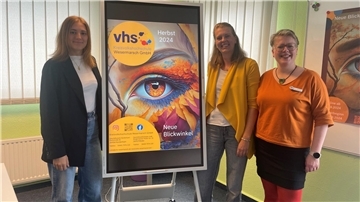 Drei Frauen vor einem bunten Plakat