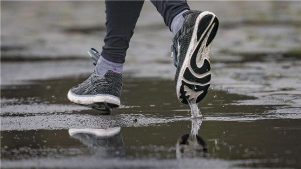 Runter vom Sofa und rein in die Sportschuhe: Laufen für die Gesundheit Die Füße eines Joggers spiegeln sich in einer Pfütze.