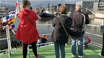 Drei Personen stehen an Bord eines Schiffes und fotografieren das Wendemanöver eines weiteren Schiffes im Neuen Hafen Bremerhaven.