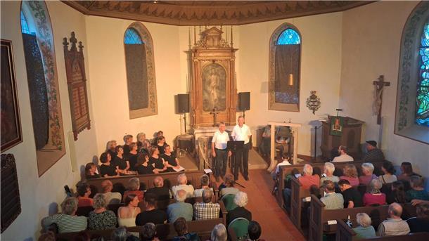 Zwei Männer stehen vor dem Kirchenaltar. Die Bänke in der Kirche sind voll besetzt. 