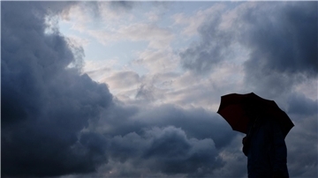 Ein Mann steht mit einem Regenschirm unter aufziehenden Wolken. 