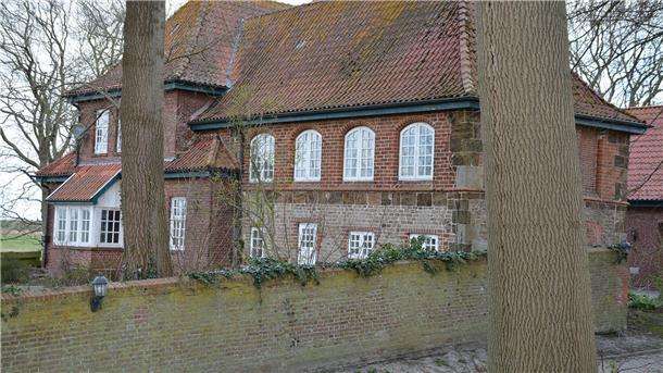 Altes Pfarrhaus, davor eine Mauer und Bäume.