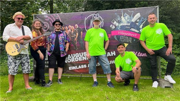 Sechs Menschen stehen auf einer Wiese vor einer Leinwand, die auf ein Festival hinweist. Das Villagemove Festival verwandelt Friedrich-August-Hütte am 2. August wieder in eine große Freiluft-Party mit Livemusik, DJs und Streetfood. Christoph Gebel, Sven Nocker, Peter Kleemann, Jan Kohet, Lisa Schlesies-Janssen und Claus Schultze (von rechts) freuen sich auf viele Besucher.