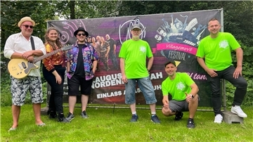 Sechs Menschen stehen auf einer Wiese vor einer Leinwand, die auf ein Festival hinweist. Das Villagemove Festival verwandelt Friedrich-August-Hütte am 2. August wieder in eine große Freiluft-Party mit Livemusik, DJs und Streetfood. Christoph Gebel, Sven Nocker, Peter Kleemann, Jan Kohet, Lisa Schlesies-Janssen und Claus Schultze (von rechts) freuen sich auf viele Besucher.