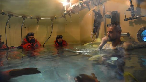 Das Wasser in der Schleuse steigt manchmal bis zum Hals. Die U-Boot-Fahrer in den Rettungsanzügen bereiten sich darauf vor, die Schleuse einzeln durch das Schott zum Tieftauchtopf zu verlassen. Ausbilder Konrad (rechts) betreut sie.