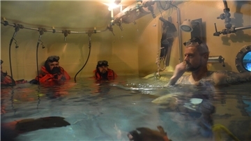 Das Wasser in der Schleuse steigt manchmal bis zum Hals. Die U-Boot-Fahrer in den Rettungsanzügen bereiten sich darauf vor, die Schleuse einzeln durch das Schott zum Tieftauchtopf zu verlassen. Ausbilder Konrad (rechts) betreut sie.