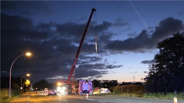 Ein mobiler Kran steht am Rande einer Straße, davor ein Fahrzueg der Feuerwehr.