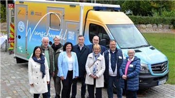 Gruppenfoto vor dem Wunschmobil des Hospizvereins Geestland: Neun Personen, darunter Projektbeteiligte und Unterstützer wie Europaabgeordneter David McAllister (Mitte), stehen lächelnd vor dem farbenfroh gestalteten Spezialfahrzeug.