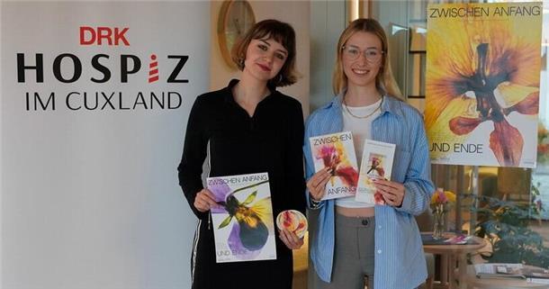 Zwei junge Frauen stehen nebeneinander vor einem Roll-up des DRK-Hospiz im Cuxland und halten Materialien der Kampagne „Zwischen Anfang und Ende“ in den Händen. Im Hintergrund ist ein farbiges Kampagnenplakat mit Blütenmotiv zu sehen.