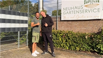 Zwei junge Herren stehen vor einem Gebäude, lächeln in die Kamera und halten einen Daumen nach oben.