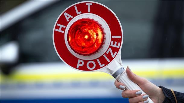 Eine Polizistin hält während einer Verkehrskontrolle eine Polizeikelle mit der Aufschrift „Halt Polizei“.