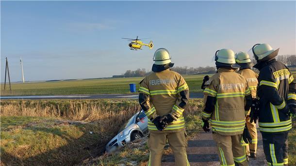 Unfall in Butjadingen: Im Hintergrund ist ein Rettungshubschrauber zu sehen, im Vordergrund Feuerwehrleute.