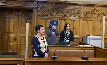 Drei Menschen stehen im Gerichtssaal, einer verdeckt sein Gesicht.
