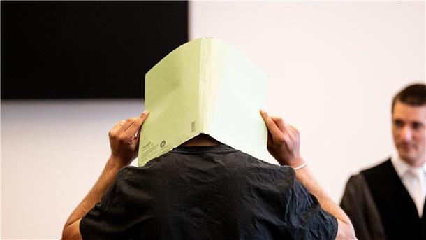Silvester-Böllerwurf: Acht Monate Haft auf Bewährung Der Angeklagte (M) verbirgt im Gerichtssaal sein Gesicht hinter einer Aktenmappe.