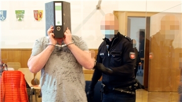 Missbrauch: Stieftochter war erst zehn Jahre alt Der Angeklagte verbirgt sein Gesicht hinter einem Aktenordner, als er zum Prozessauftakt von einem Justizvollzugsbeamten an seinen Platz geführt wird. Schoener