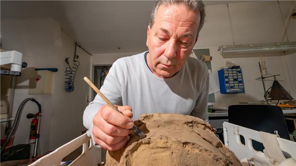 Ein Mann pinselt Sand von den Überresten einer Urne. 