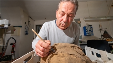 Ein Mann pinselt Sand von den Überresten einer Urne. 