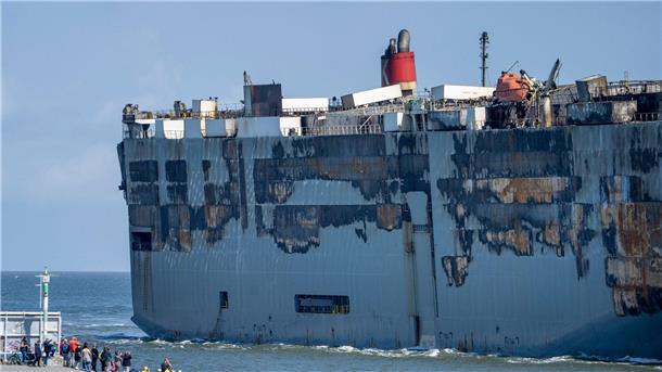 Nach Großfeuer: Beschädigter Frachter im sicheren Hafen Der Autofrachter „Fremantle Highway“ wird an Schaulustigen vorbei in den Hafen gezogen.