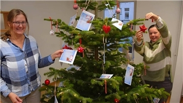 Zwei Frauen stehen an einem Weihnachtsbaum mit Wunschkarten