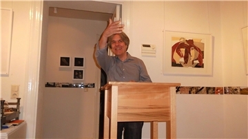 Ein Mann steht an einem Rednerpult und hebt grüßend die Hand. 