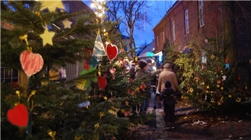 Bunte Papieranhänger schmücken die Tannenbäume in einer Seitenstraße, dazwischen schlendern Menschen hindurch.