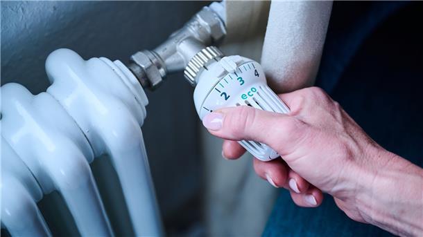 Eine Frau dreht den Temperaturregler einer Heizung auf 3