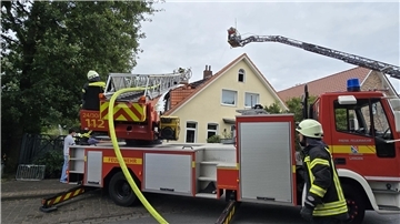 Eine Feuerwehr-Drehleiter steht vor einem Wohnhaus mit Ziegeldach, das rote Ziegeldach ist nach einem Feuer aufgerissen