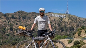 Der deutsche Athlet Jonas Deichmann mit seinem Fahrrad vor der Kulisse der Hollywood Hills in den USA.