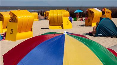 Bürger aus Wurster Nordseeküste kommen bald umsonst an Cuxhavens Strände Ein bunter Sonnenschirm im Vordergrund, dahinter Sandstrand, gelbe Strandkörbe und Menschen, verschwommen.