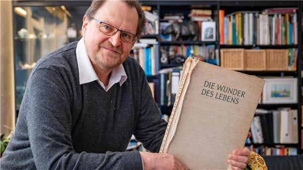 Ein Mann hält das Buch "Die Wunder des Lebens" in der Hand.