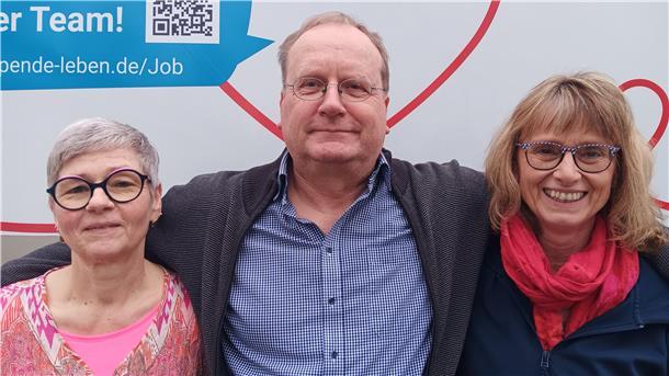 Zwei Frauen und in der Mitte ein Mann lächeln in die Kamera.