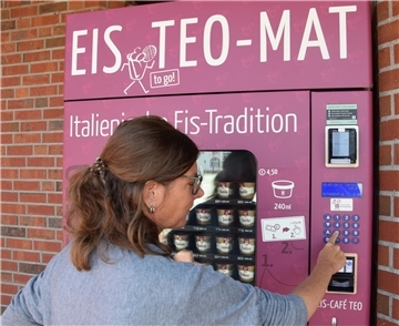 Eine Frau steht am Automaten und zieht ein Eis. 