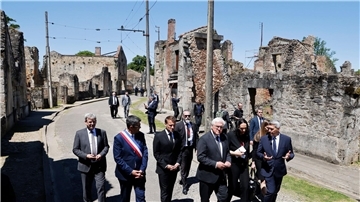 Der französische Präsident Emmanuel Macron und der deutsche Bundespräsident Frank-Walter Steinmeier gehen an Ruinen in Oradour-sur-Glane vorbei.