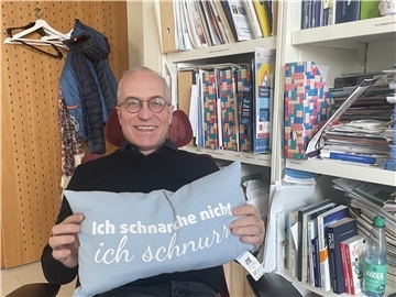 Mann sitzt auf einem Stuhl und hält ein Kissen in der Hand.