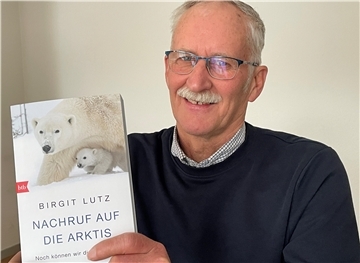 Ein Mann zeigt das Buch  "Nachruf auf die Arktis". auf dem Titel ist ein eisbär zu sehen.