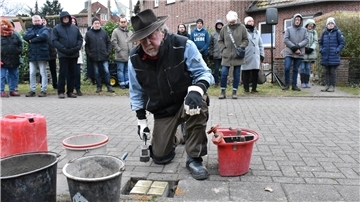 Ein alter Mann kniet auf einer Straße und verlegt Pflastersteinen.