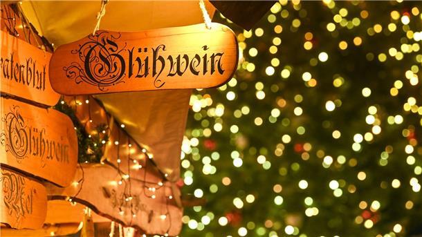 Ein Holzschild mit der Aufschrift „Glühwein“ hängt an einem Marktstand.