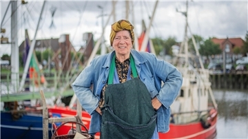 Frau steht kostümiert in einem Kutterhafen