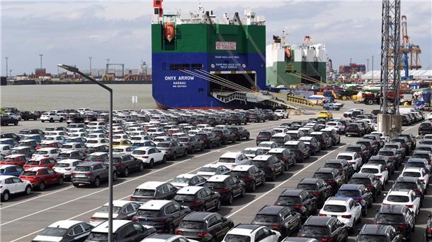 Autos im Hafen stehen vor einem Autotransporter