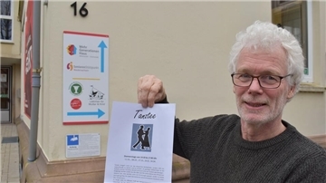 Ein Mann steht vor dem Mehrgenerationenhaus in Nordenham und hält ein bedrucktes Blatt Papier in die Kamera.