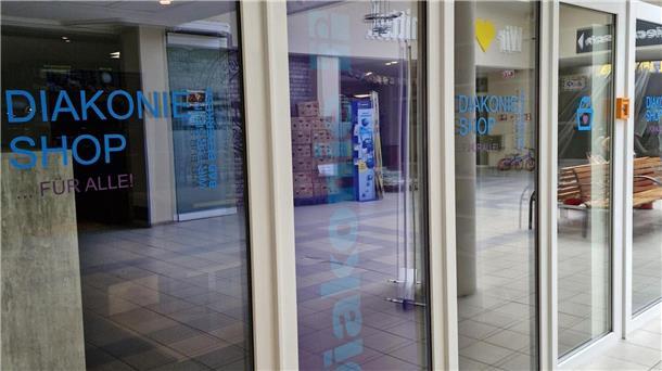 Außenansicht des neuen Diakonie-Shops in der Rolandpassage in Bad Bederkesa mit Glasfassade, blauer Aufschrift „Diakonie Shop … für alle!“ und Blick ins Innere.
