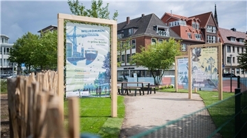 Der neue Infoplatz auf dem ehemaligen Finanzamtsgelände hat Gestalt angenommen mit Infostelen, Tischen, Bänken und drei Bäumen.