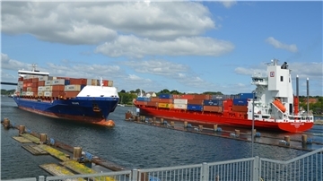 Zwei Schiffe fahren vor einer Schleusenanlage im Nord-Ostsee-Kanal aneinander vorbei. 