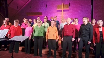 Der Popchor „nach acht“ singt beim Jubiläumskonzert in der St.-Petri-Kirche Langen. Die Sängerinnen und Sänger stehen vor beleuchtetem Altar, viele tragen bunte Oberteile.