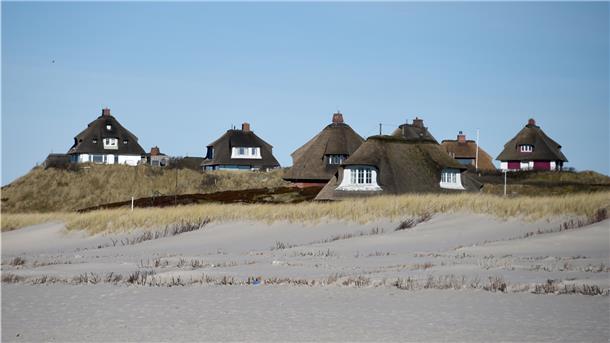 Typische Sylter Reetdachhäuser sind hinter dem Strand von Hörnum auf Sylt zu sehen.