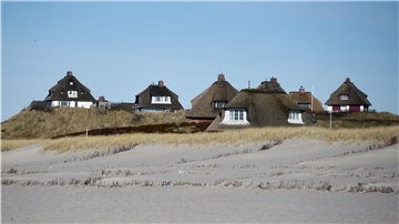 Typische Sylter Reetdachhäuser sind hinter dem Strand von Hörnum auf Sylt zu sehen.