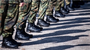 Beine und Füße von Soldaten. Sie stehen auf der Straße, der Bildausschnitt zeigt die militärische Kleidung und Schuhe.